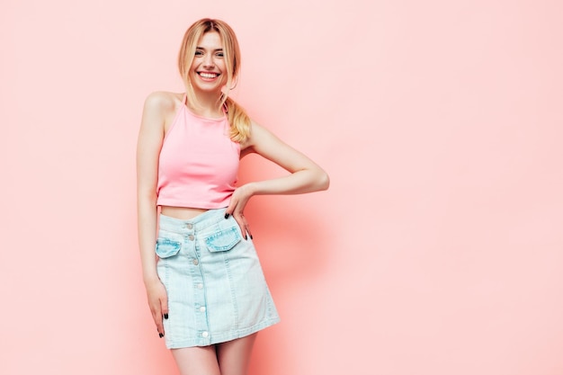 Free photo back of young beautiful smiling blond female in trendy summer clothes sexy carefree woman posing near pink wall in studio positive model having fun indoors cheerful and happy