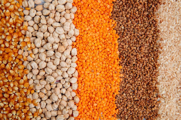 Background of different types of groats corn seeds chickpeas red lentils buckwheat and rice top view