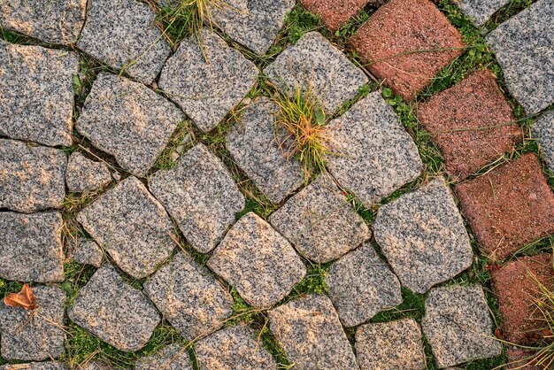 Background of gray small paving stones with sprouted grass between the stones top view of the path refreshed by the sun idea for background or wallpaper