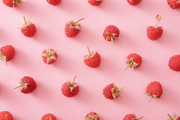 Background pattern of luscious ripe red raspberries arranged scattered on pink paper viewed from above