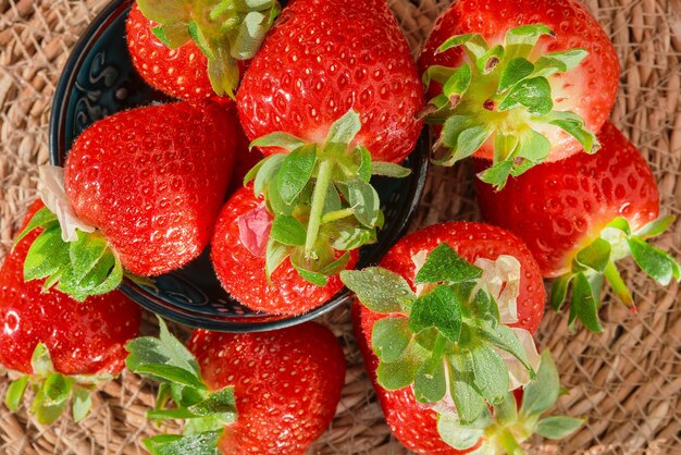 Background of strawberries with water drops in a bowl top view of a harvested berry on a straw lining natural sunlight strawberry spring season