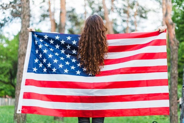 自然の中でアメリカの旗を持つ女の子のバックビュー