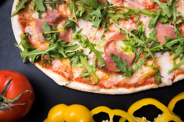 Bacon and arugula leaves pizza with slices of yellow bell pepper and tomato