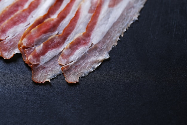 Free photo bacon on black stone plate, top view