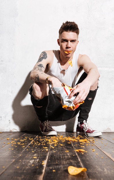 Бесплатное фото Плохой человек с татуировкой ест чипсы из пакета