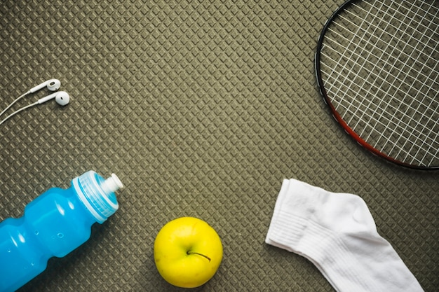 Foto gratuita badminton; mela; calzino; bottiglia d'acqua e auricolare sul fondo del modello strutturato