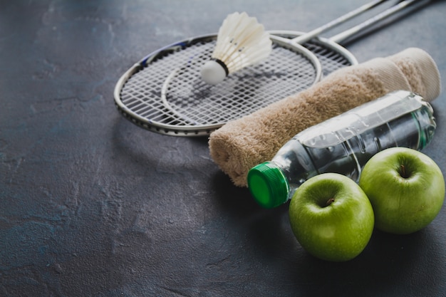 Free photo badminton rackets with apples and water bottle