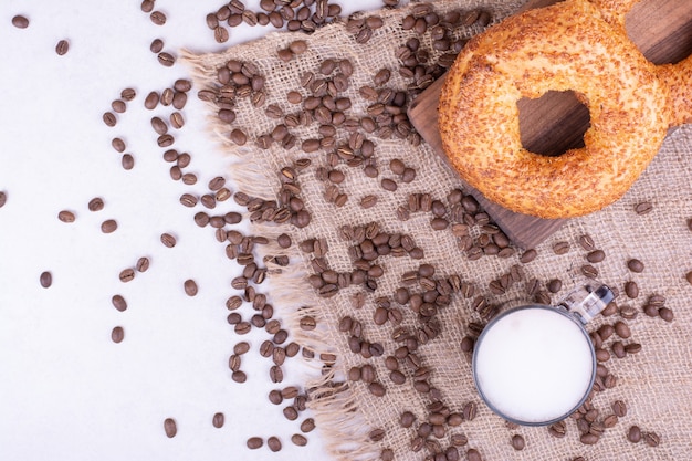 Foto gratuita bagel con un bicchiere di bevanda e fagioli arabica intorno