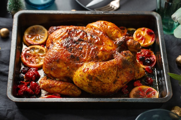 Baked appetizing whole chicken with oranges and cranberries in oven form. Closeup