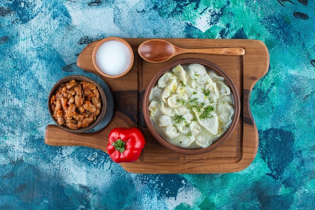 Baked beans, dushbara, spoon, pepper and salt on a board, on the blue table. 