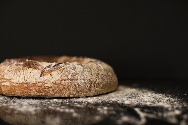 Baked bread bun dusted on flour against black background