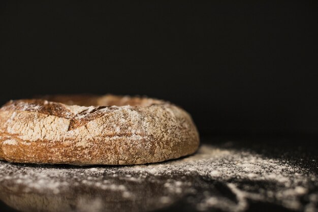 Baked bread bun dusted on flour against black background