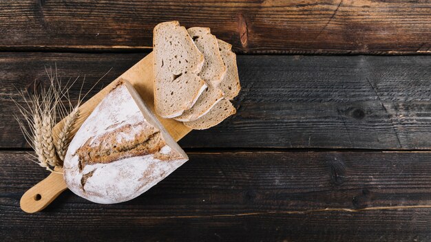 Baked bread and ear of wheat on chopping board over the wooden table