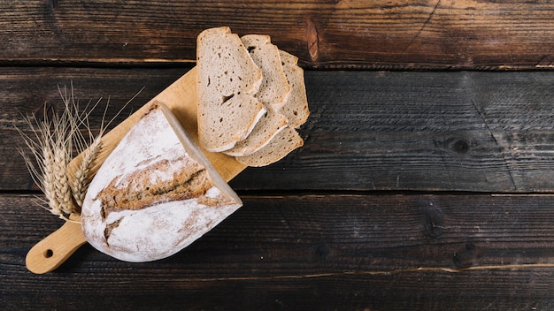 Запеченный хлеб и ухо пшеницы на разделочной доске над деревянным столом