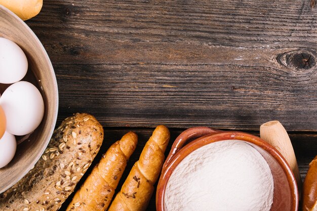 Baked bread; flour and eggs in bowl on wooden textured backdrop