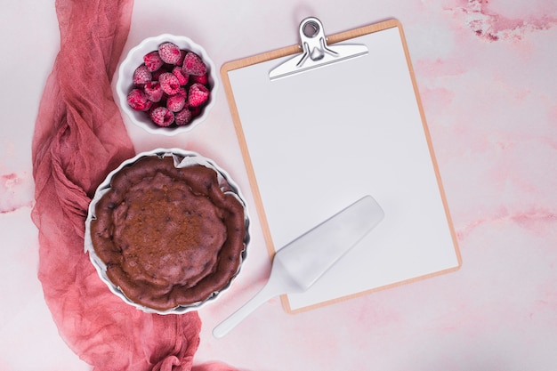 구운 케이크; 산딸기; 분홍색 질감 된 배경 위에 백서와 클립 보드에 주걱