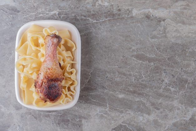 Baked chicken drumstick over pasta , on the marble background.