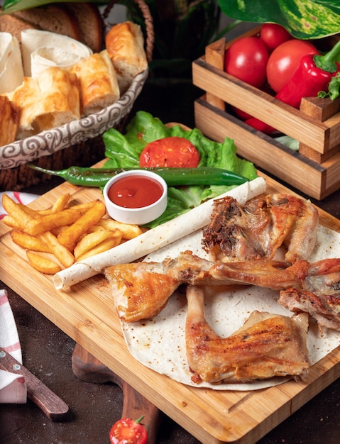 Baked chicken wings with French fries in lavash with vegetables and ketchup on wooden board