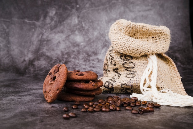 Baked cookies and roasted coffee beans with sack on rustic backdrop