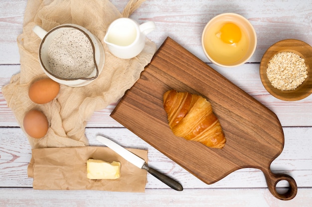 Baked croissant on chopping board with ingredients on wooden plank