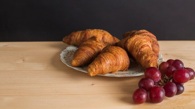 Baked croissants on ceramic plate and ripe grapes on wooden table