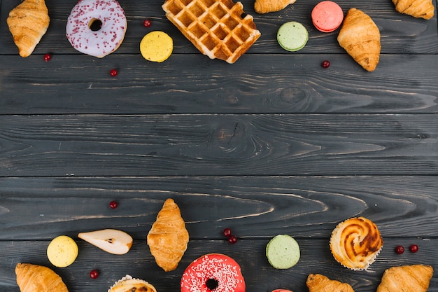 Baked croissants; macaroons; donuts and cupcakes on wooden textured backdrop