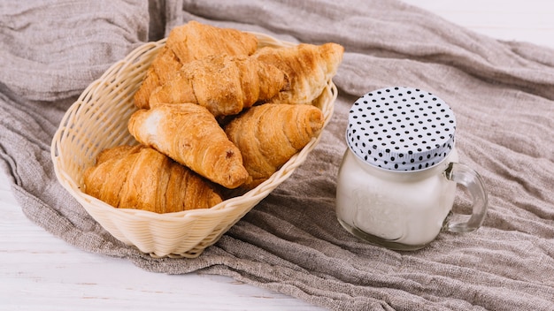 Baked croissants and milk in closed mason jar on crumpled sack textile