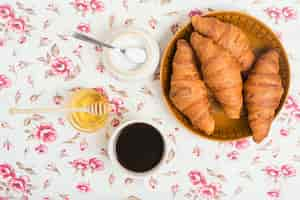 Free photo baked croissants; tea; honey and powdered milk on floral background