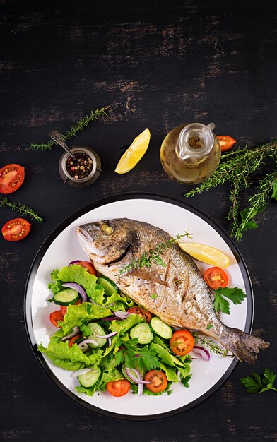 Baked fish dorado with lemon and fresh salad in white plate