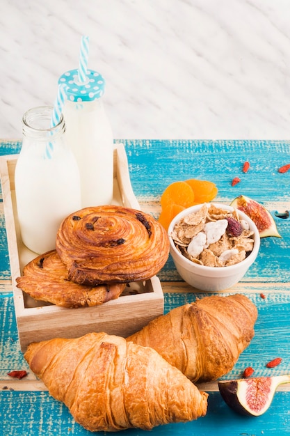 Baked food with milk bottles; bowl of corn flakes fig fruit slices and dry apricot over wooden desk