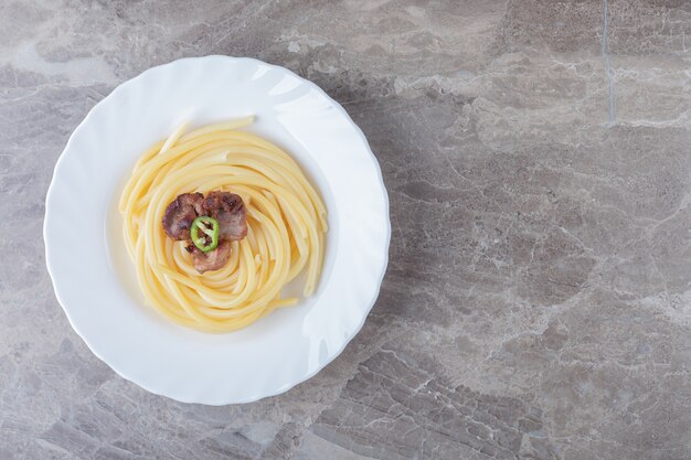 大理石の表面にある皿の上のパスタの上に焼いた肉。