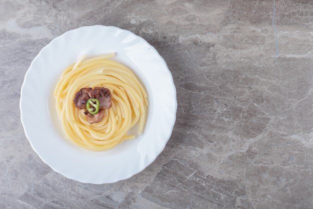 Baked meat over pasta on the plate , on the marble surface.