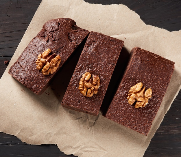 Запеченные кусочки шоколадного торта брауни с орехами на коричневом листе бумаги