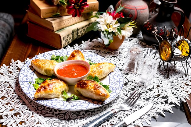 Baked stuffed pastry with sesame sprinkles served with tomato sauce