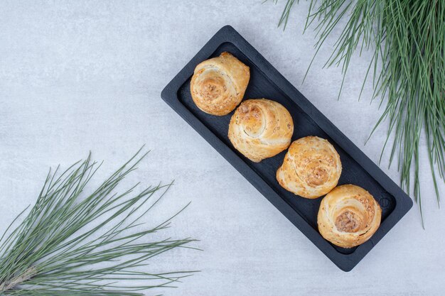 Baked sweet rolls on black plate with pine tree branch. High quality photo