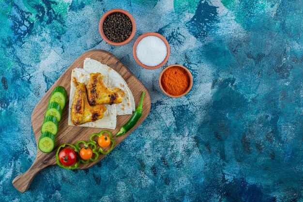 Baked wings, lavash and vegetables on a cutting board, on the blue background. 