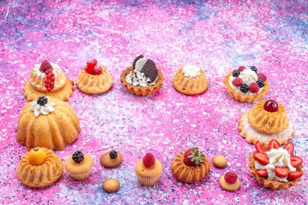 запеченные вкусные пирожные со сливками вместе с разными ягодами на светлом-ярком столе, бисквитный ягодный сладкий запеканный чай