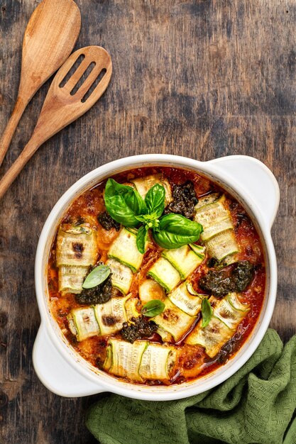 イタリア風の木製の背景にマリナラソースでリコッタとチーズを入れた焼き zucchiniロール