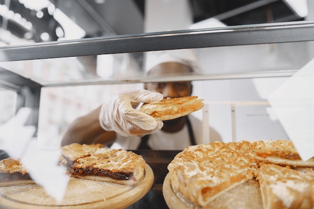 Baker arranging showcase in bakery. Selling product to a customer.