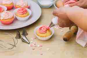 Free photo baker decorates muffins with cream over the wooden desk