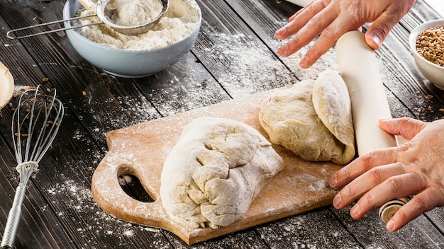 Free photo baker flattening the dough with rolling pin on chopping board