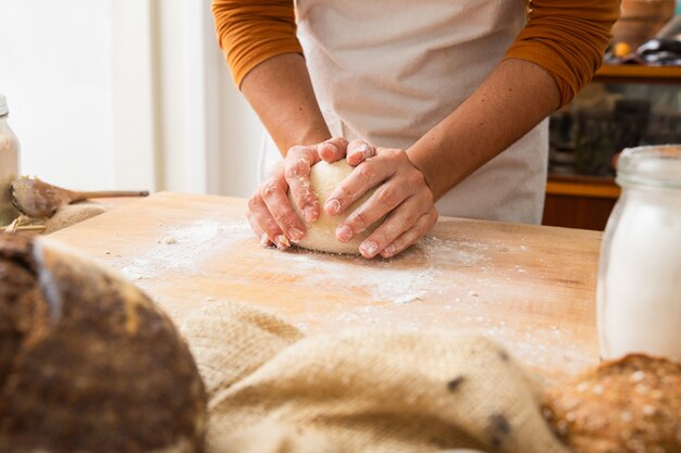 Baker forming dough in sphere on wooden board