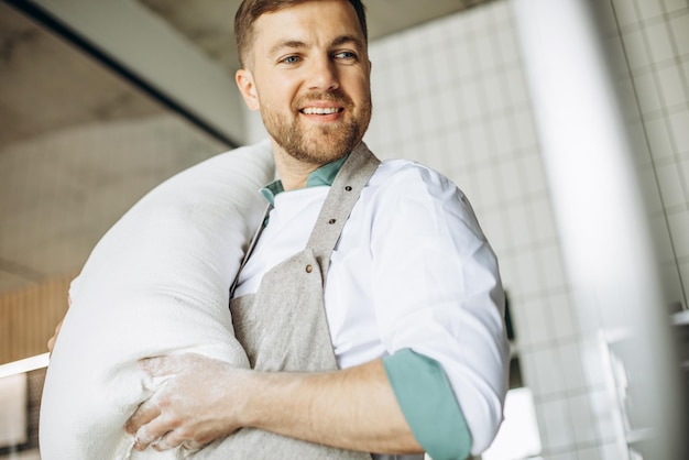 Foto gratuita baker che tiene un grande sacco di farina in cucina nella casa del forno