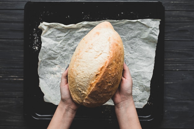 Free photo baker holding bread loaf above table