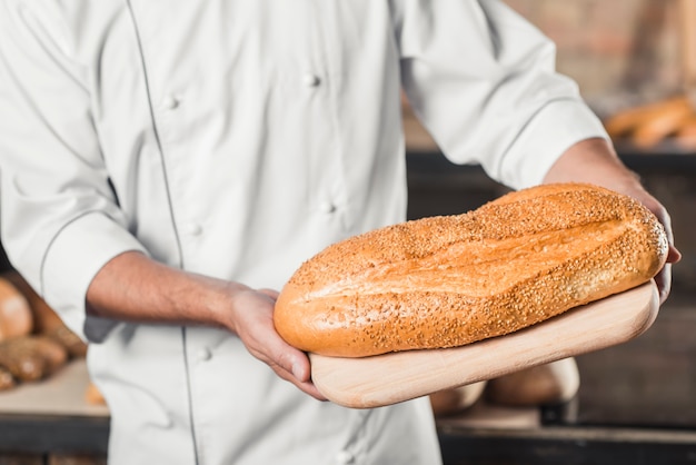 Free photo baker holding fresh baked bread on chopping board