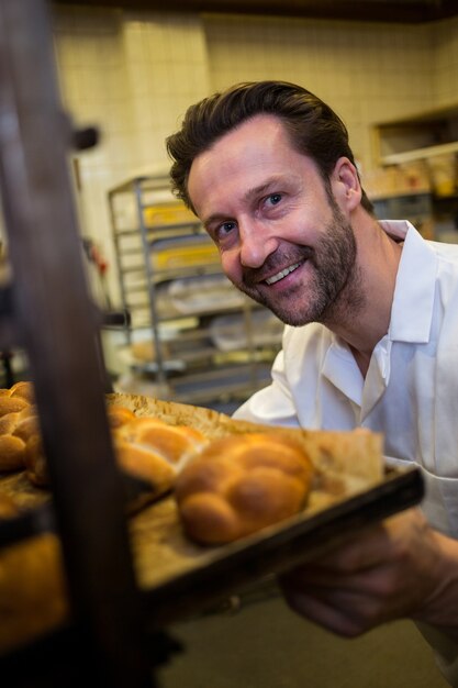 Baker keeping tray of baked buns in shelf