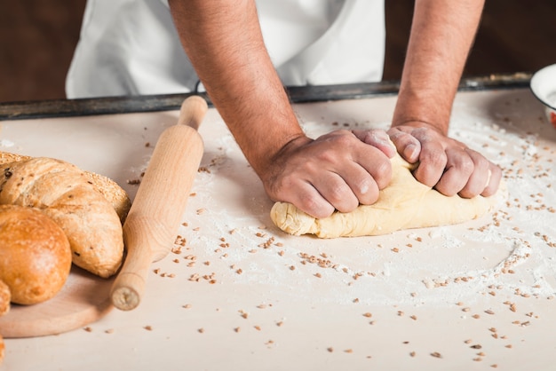 Baker kneading bread dough on table