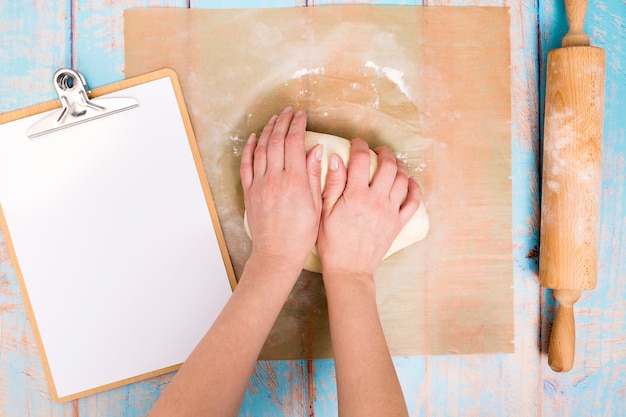 Baker kneading the dough on parchment paper with clipboard and rolling pin on table