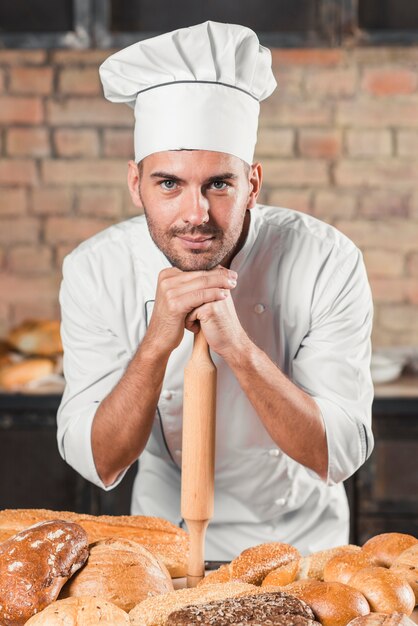 Baker leaning on rolling pin over the table with variety of breads