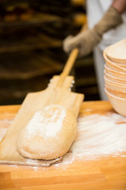 Baker lifting bread dough in wooden spoon